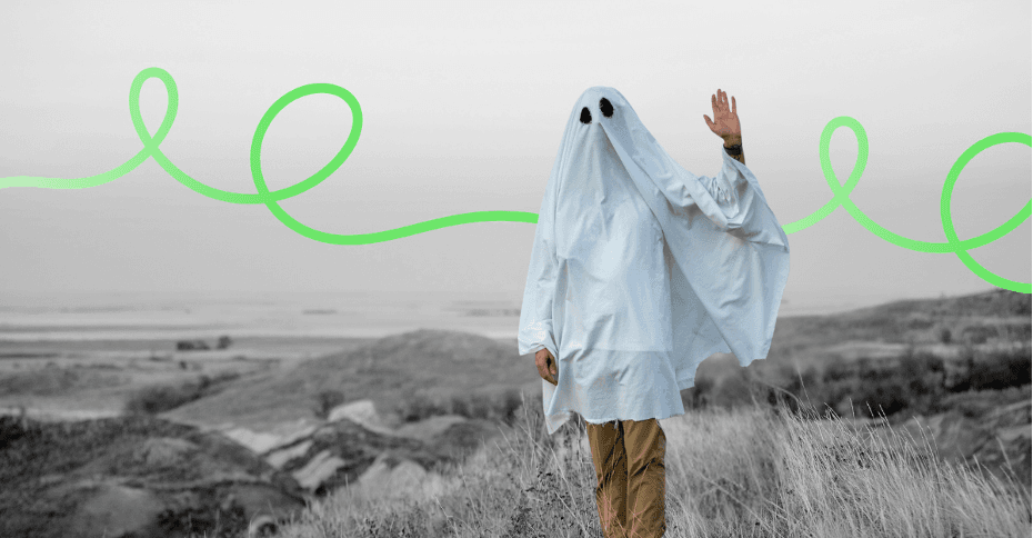A person under a white sheet dressed as a ghost, waving in an open field.