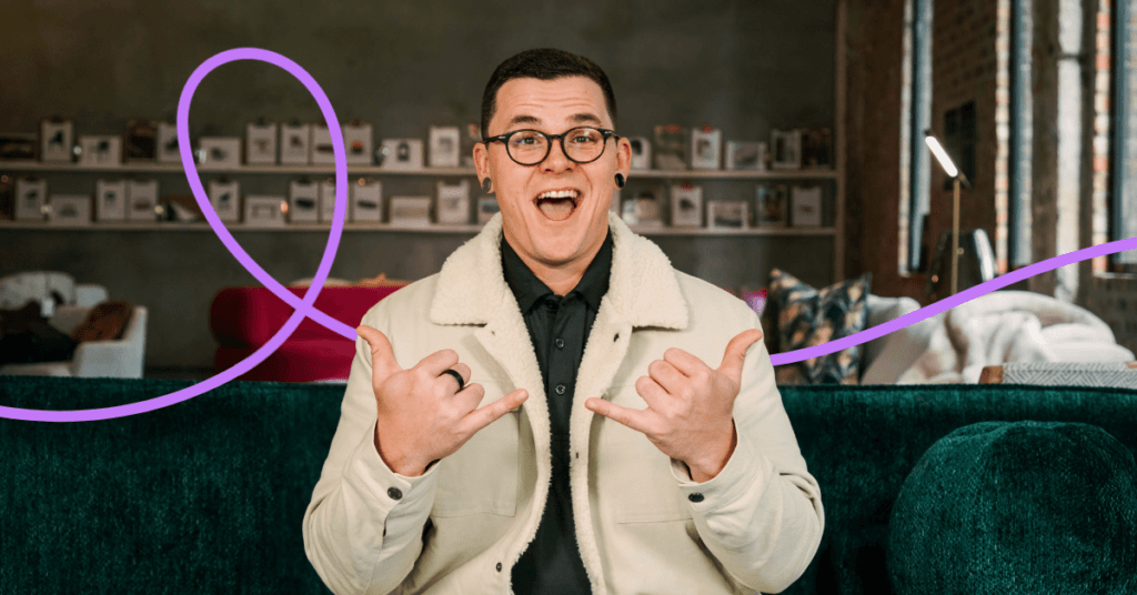 A man in a cream jacket grinning and pointing both thumbs at himself.