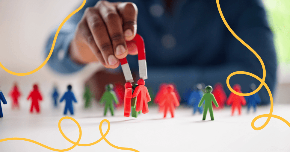 A hand holding a magnet above a group of small coloured figures, drawing some of them in.
