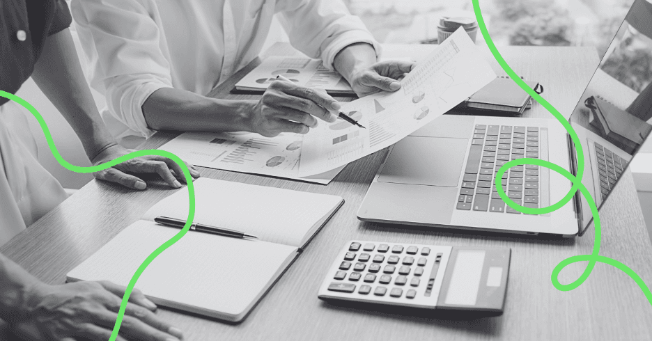 An overhead view of a desk covered in printed charts, a calculator, a laptop and notebooks.